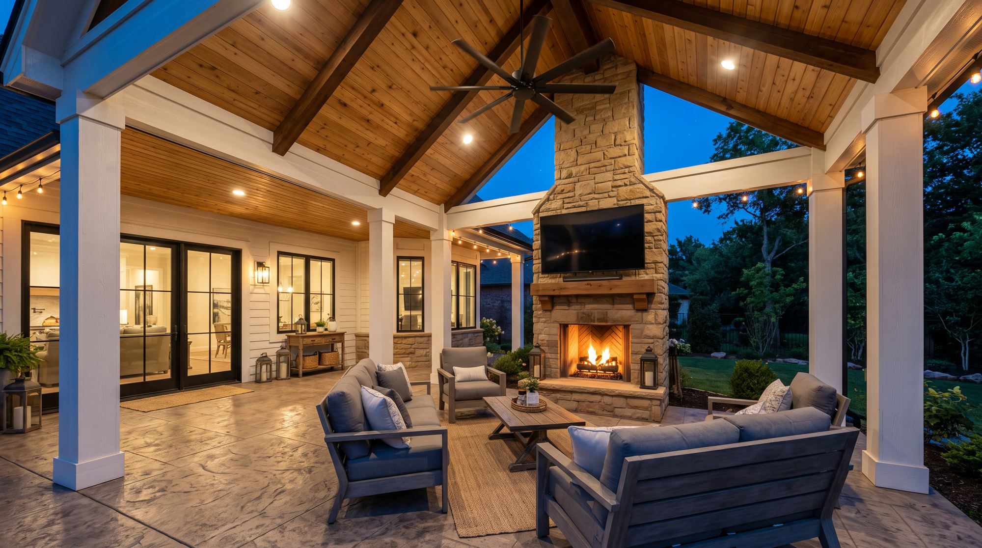 Covered patio with stone fireplace and cedar ceiling at dusk